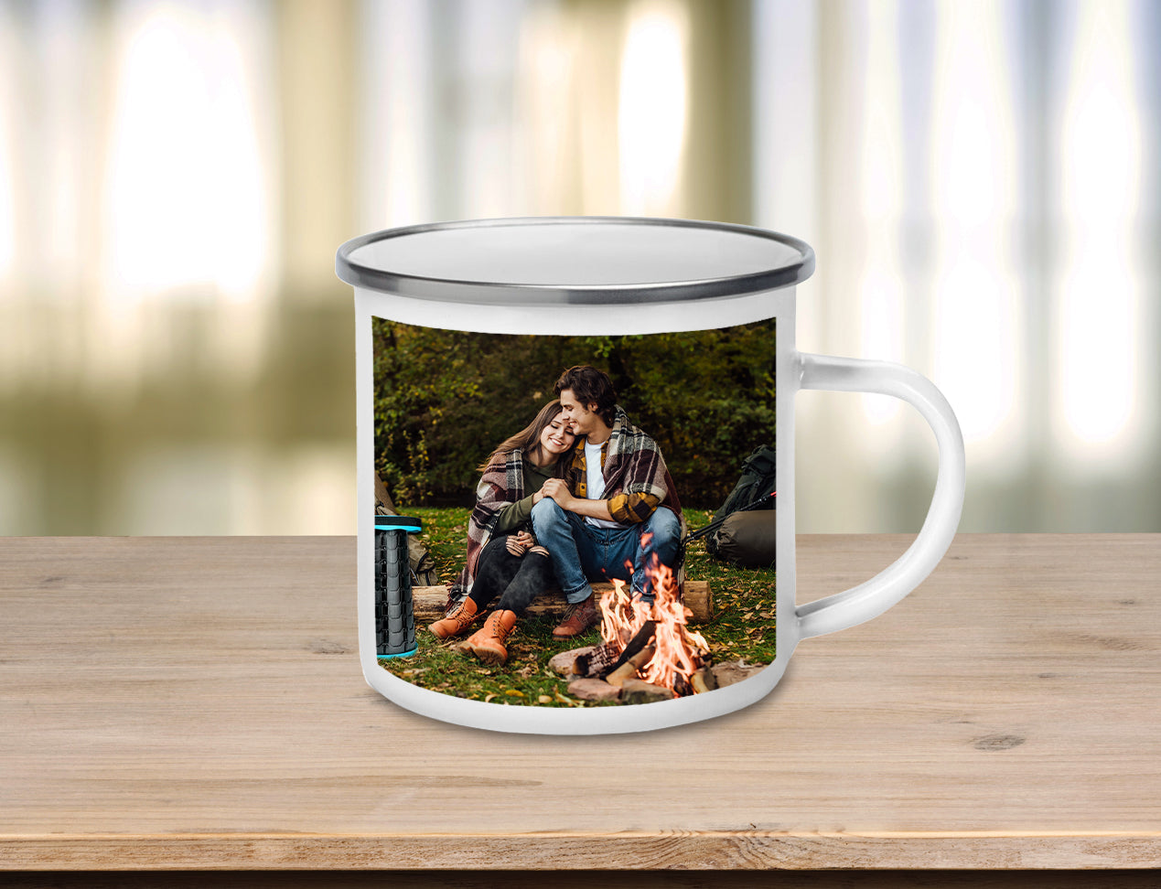 Custom Enamel Mug sitting on table, personalised with photo of couple near camp fire.