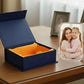 Stylish blue gift box with orange interior on a wooden surface, next to a glass photo block with a family photo.